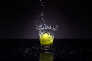 a yellow ball dropped into a glass of water against a black background