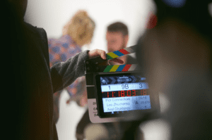 on the set of a corporate video with people out of focus and a hand holding a digital slate