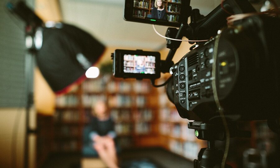 camera on set in a library filming an interview
