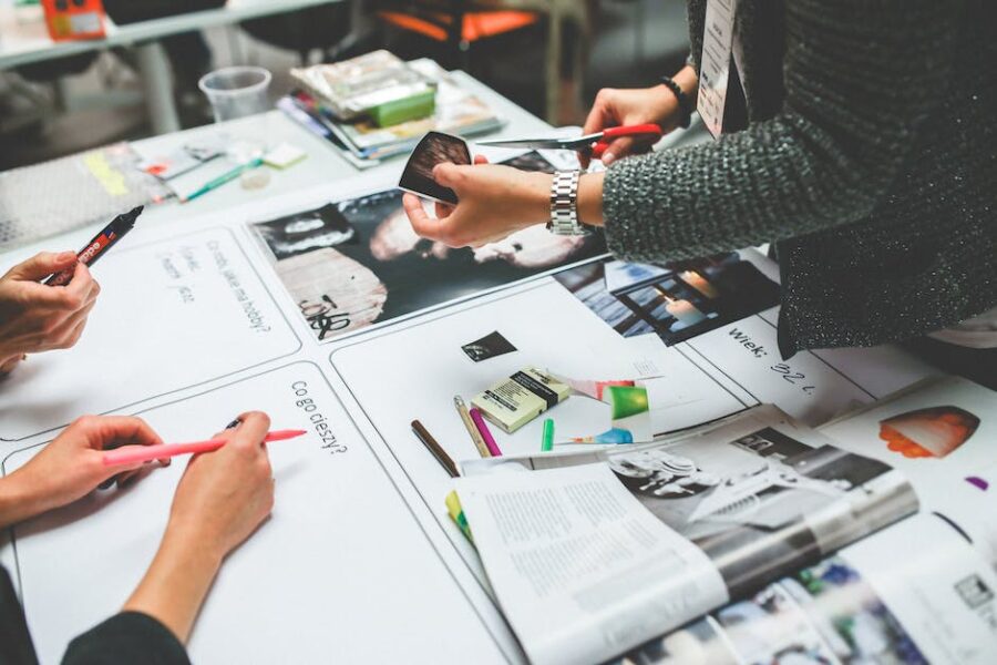 people working over a table on a project with lots of paper and office products