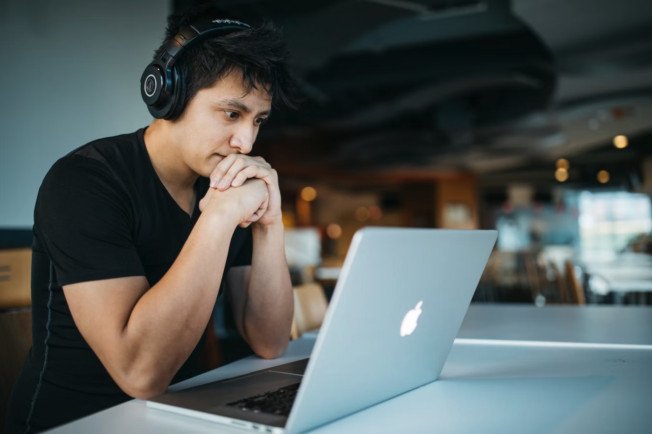 man in 20s with headphones on watching laptop inside office common room