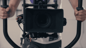 camera operator holding a camera in a handheld rig facing you