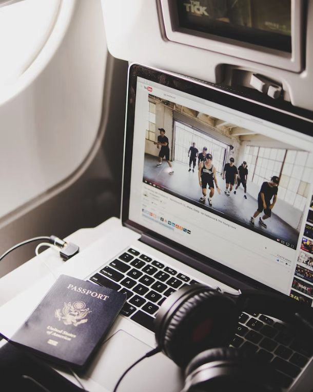 laptop sitting on an airplane table with headphones and a passport on the keyboard, playing a youtube video