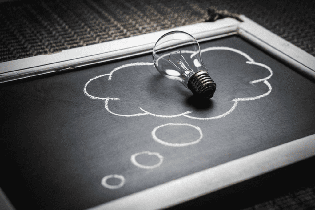 lightbulb sitting on a chalkboard with a think bubble written on it 