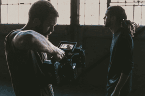 camera operator shooting a brand video, filming a man in an empty, dark warehouse