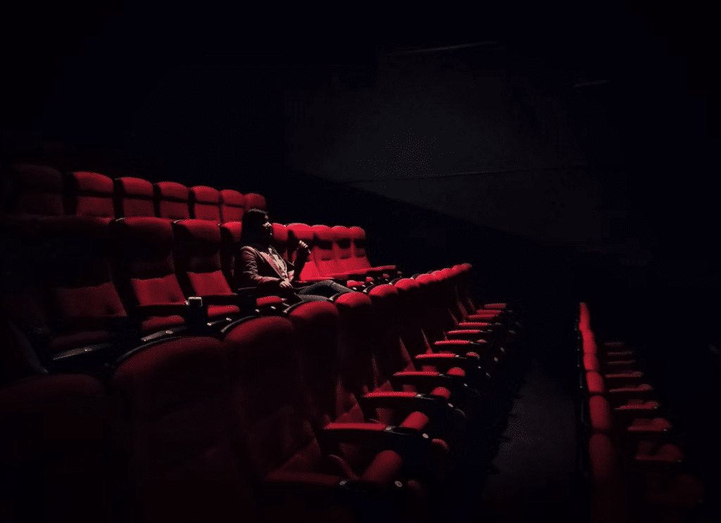 man sitting along in a dimly lit movie theater 