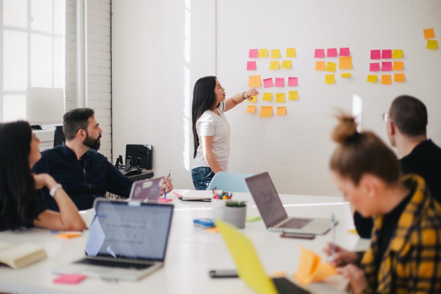 Woman in front of whiteboard speaking to a room full of people