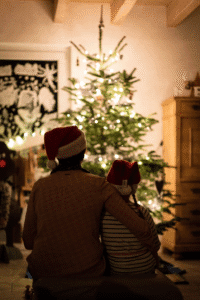 Parent and child wearing Santa hats sitting together in front of a Christmas tree