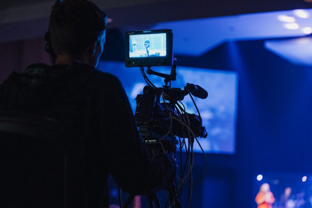Videographer operating a professional camera during a live event with blue stage lighting